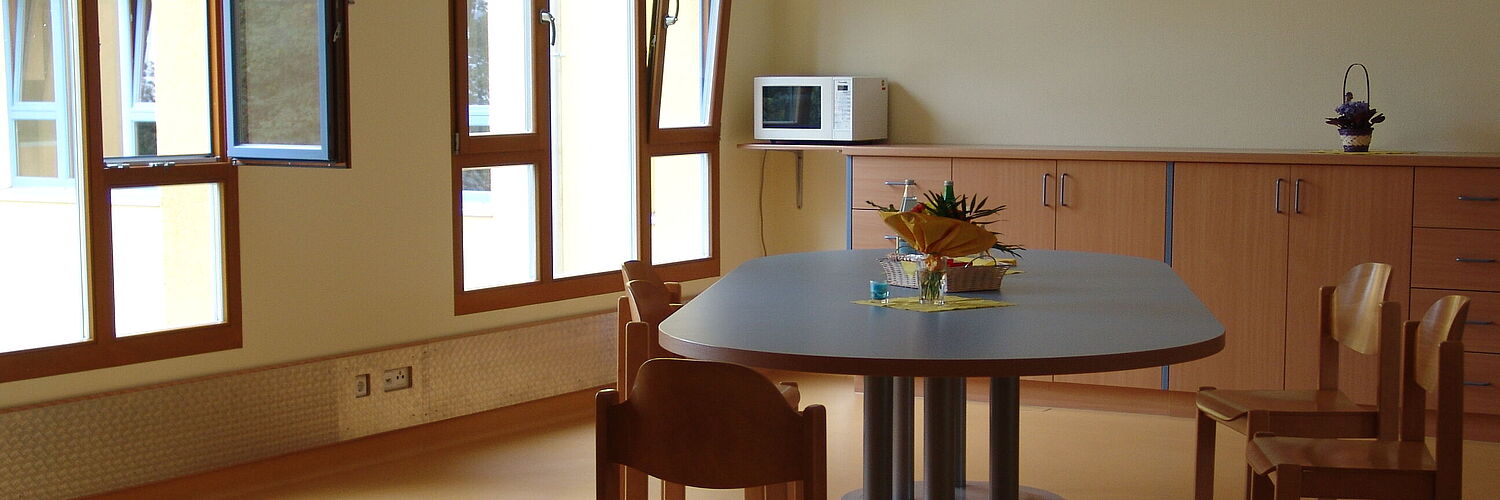 Das Bild zeigt einen Raum mit einem Tisch und Stühlen.
