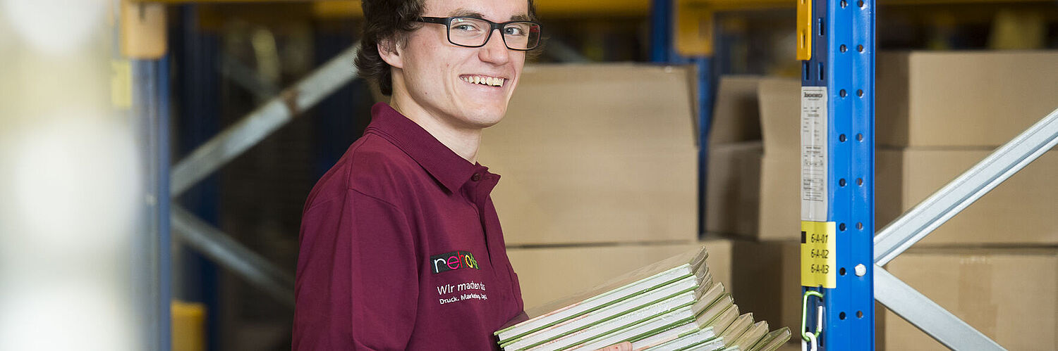 Das Bild zeigt einen Mitarbeiter mit einem Stapel Bücher in der Hand.