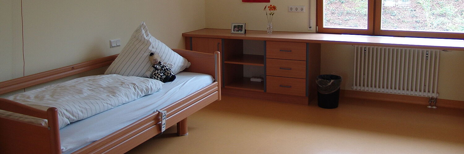 Das Bild zeigt ein Zimmer mit einem Bett und einem Schreibtisch und Fenster.